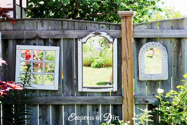 Three white framed mirrors on garden fence.