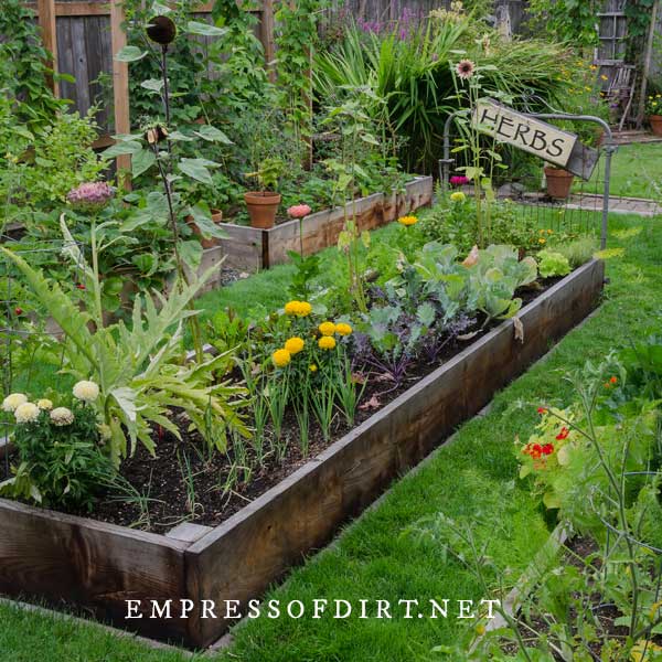 Raised garden bed with vegetables and flowers and an old garden gate with a sign saying Herbs.