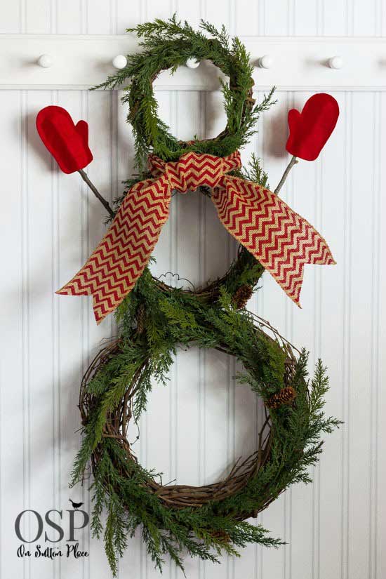 Snowman wreath made from green wreaths, mittens, and a ribbon scarf.