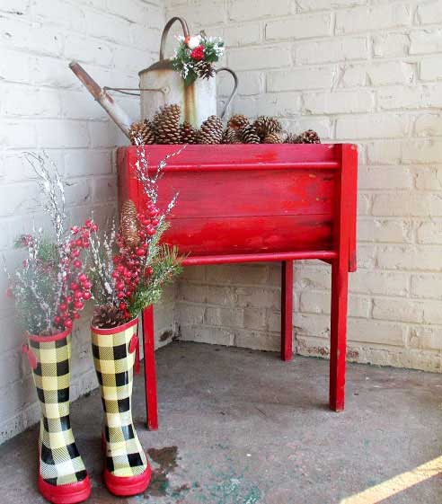 Front porch decorated for winter with a red planter box, greenery, and colorful garden boots.