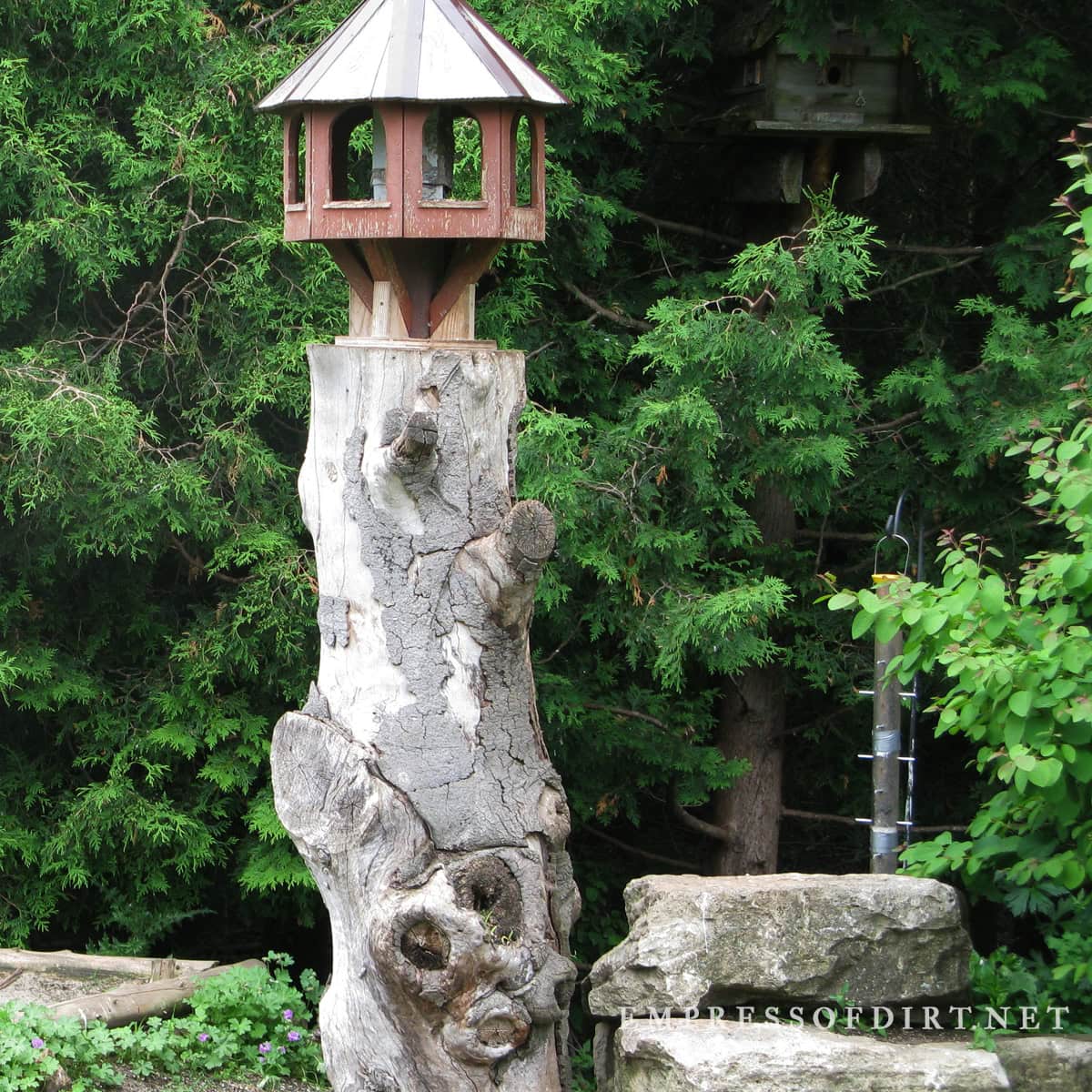 Old wood stump with round birdhouse on top.